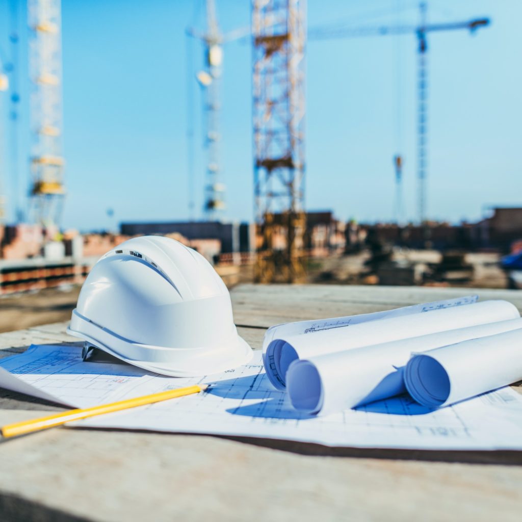 close-up shot of rolls of papers with building plans and hardhat at construction site