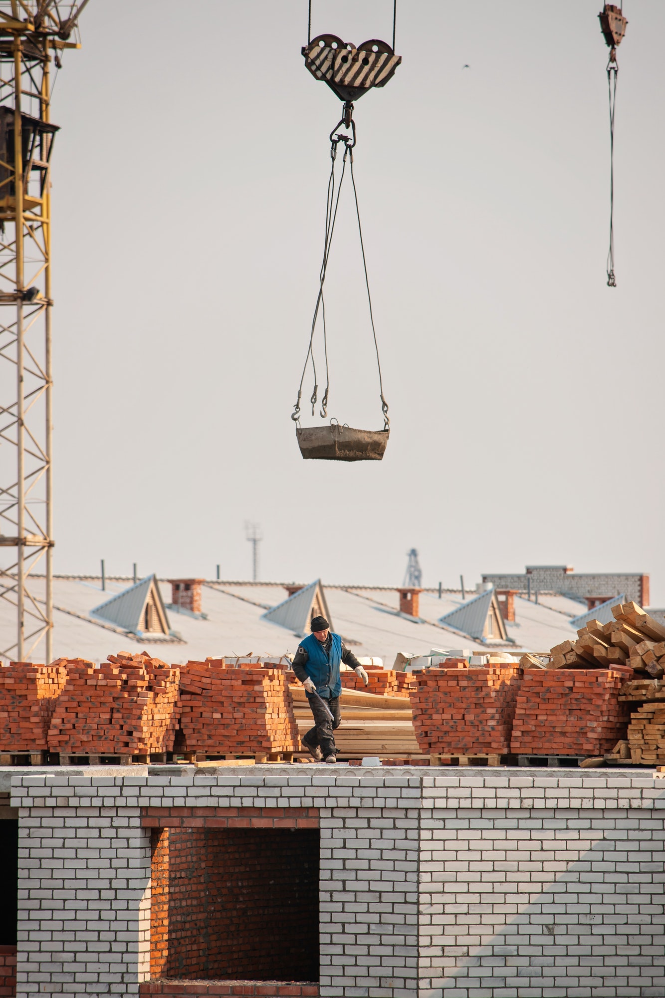 Construction. A man builder walks on the roof of a brick building under construction next to a crane