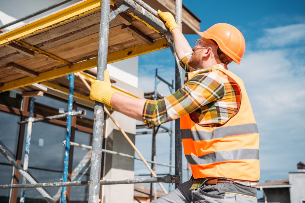 handsome builder climbing on scaffolding at construction site